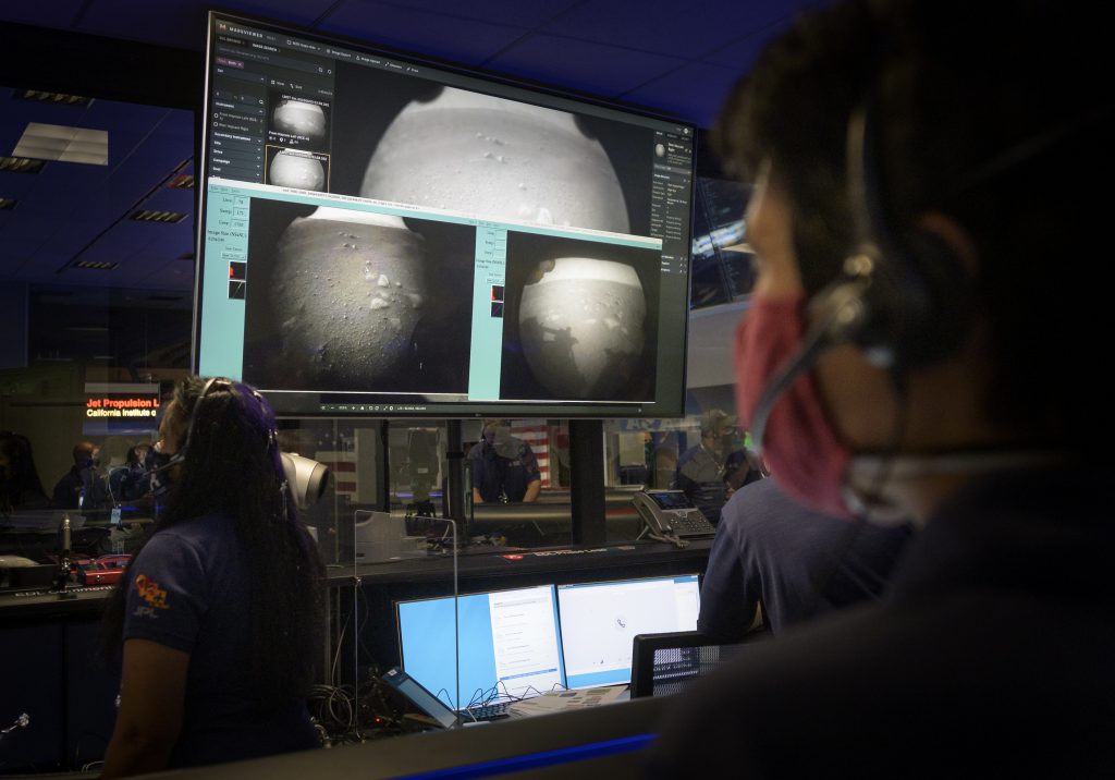 Members of NASA’s Perseverance Mars rover team watch in mission control as the first images arrive moments after the spacecraft successfully touched down on Mars, Thursday, Feb. 18, 2021, at NASA's Jet Propulsion Laboratory in Pasadena, California. A key objective for Perseverance’s mission on Mars is astrobiology, including the search for signs of ancient microbial life. The rover will characterize the planet’s geology and past climate, pave the way for human exploration of the Red Planet, and be the first mission to collect and cache Martian rock and regolith
